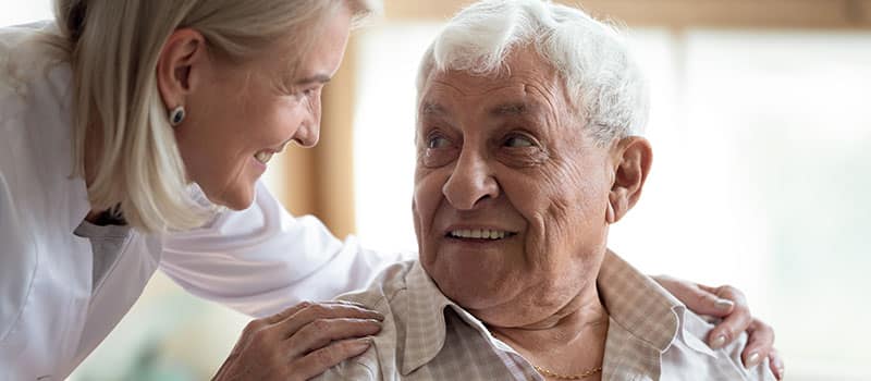 Close up middle-aged female doctor supporting older patient, touching shoulders, giving psychological help, caring mature female wearing white uniform talking with elderly man