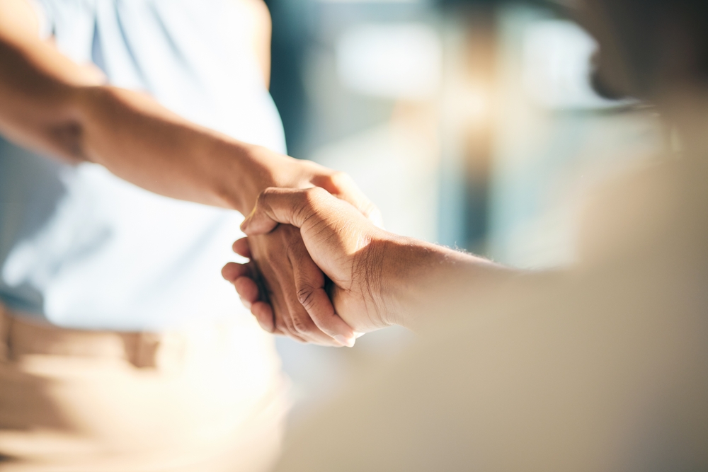 Two professionals shaking hands in a modern office, symbolizing collaboration