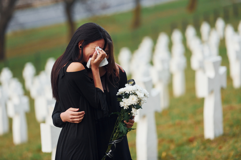 Two young women in black embracing and crying — symbolizing grief and loss due to asbestos-related illness.