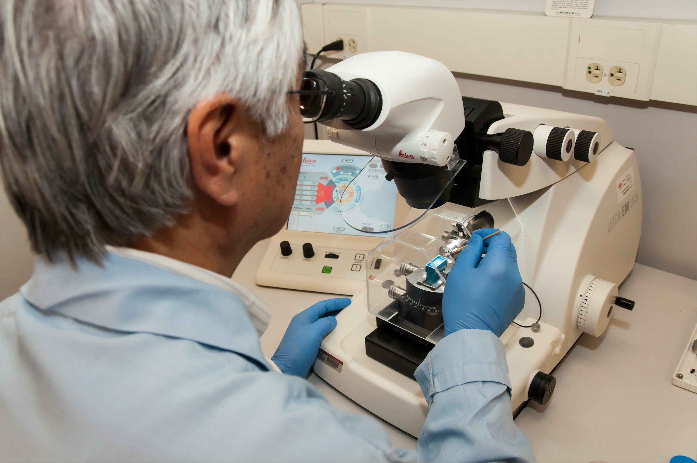 Scientist wearing gloves analyzing tissue samples using an advanced microscope in a laboratory setting