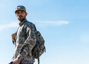 Soldier in uniform standing in a field, holding a folded American flag, representing military service and honor.